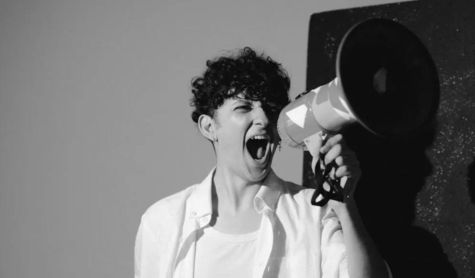 Man in white collared shirt shouting into a megaphone for article on hate speech legislation in the uk